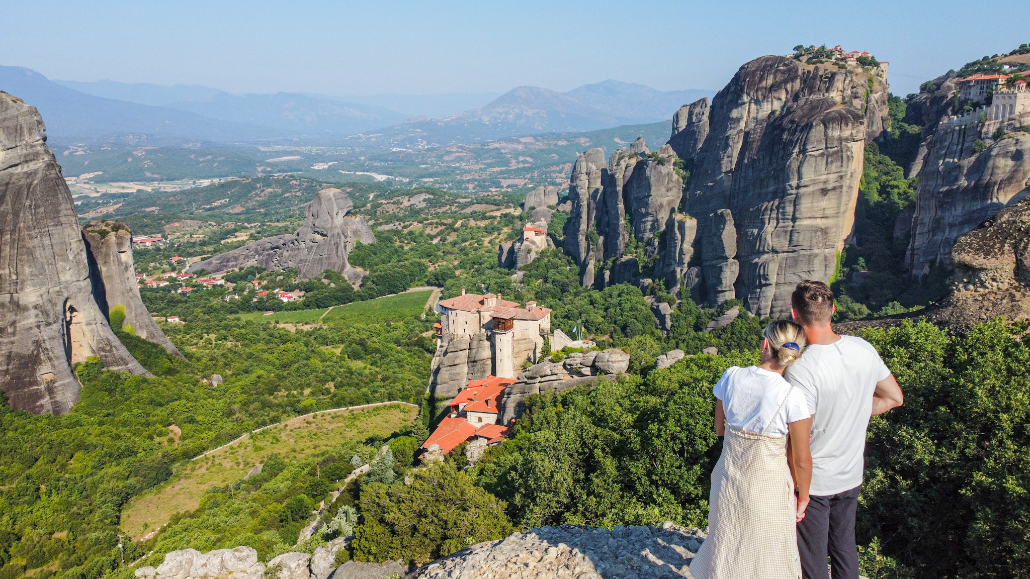 Couple holding hands and looking out at the monasteries and cliffs while visiting meteora, greece