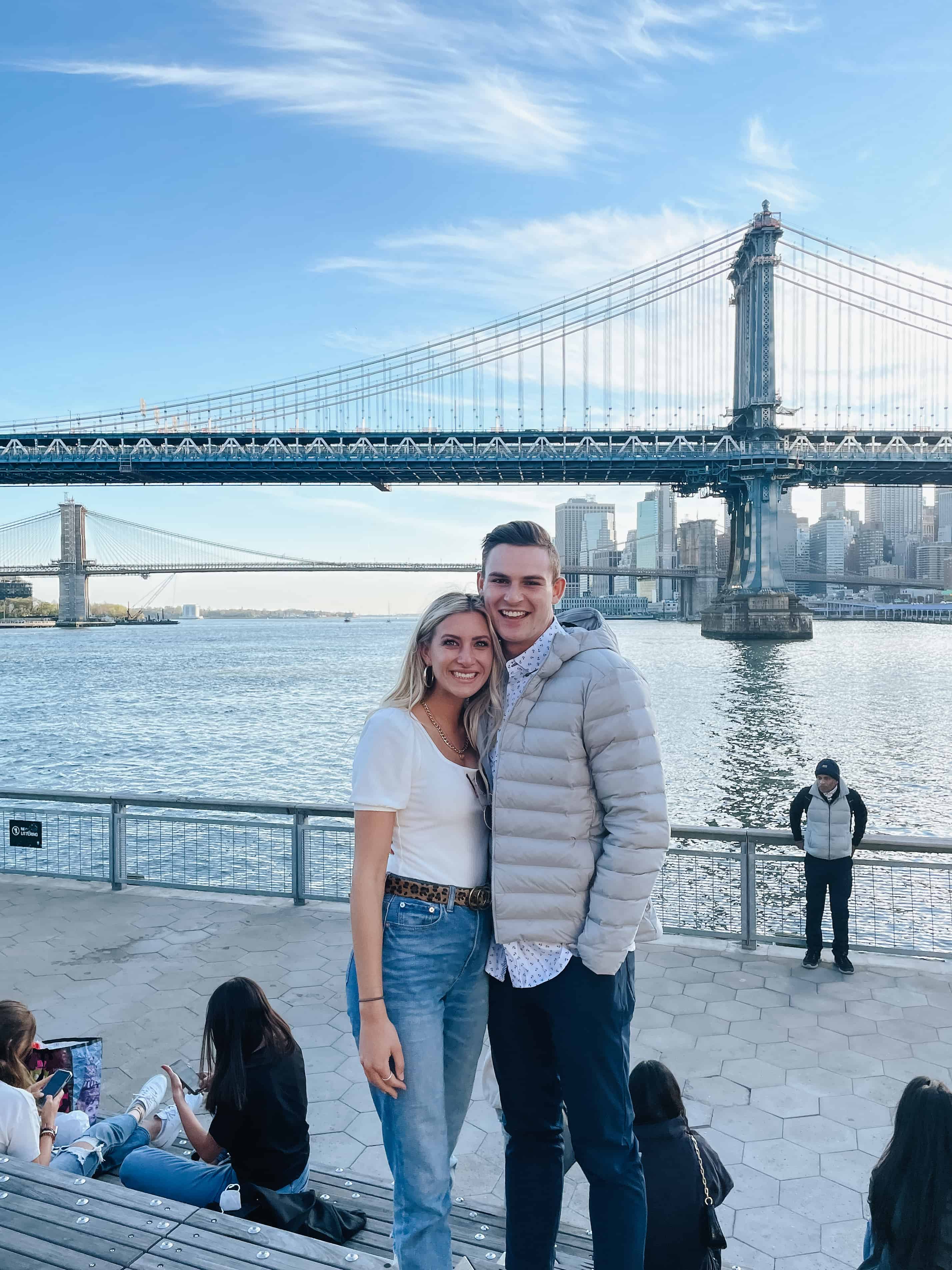 rachel and jason travelling to New York in front of the skyline and bridge